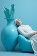 © sunaiart - Blue rhapsody.The woman is resting in a chair next to a large vase.Minimal art,rest  and interior concept.Copy space,top view.Generative AI