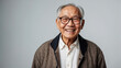 An elderly Asian happy man wearing eyeglasses on a gray solid background with copy space.