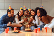 © Prostock-studio - Diverse friends embracing birthday guy sitting with party hats indoors