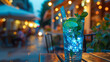 A blue mojito cocktail on a wooden table with soft terrace lights at dusk.