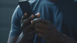 © MP Studio - A close-up of a hand holding a smartphone in a dimly lit room, with a focus on the phone screen and the glow it casts on the fingers.