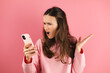 Mad and shock young brunette beautiful woman using mobile phone isolated on pink background. Yelling unhappy woman hold mobile phone. Disappointed sad upset lady horrified impressed news. WTF. Oh no.