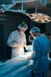 © dikushin - Vertical shot of team of professional surgeons performing invasive surgery on patient lying in hospital operating room. Surgeons using instruments. Dark and cold atmosphere. Concept of emergency.