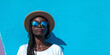 African American bright girl in sunglasses next to a skateboard in a hat stands near a bright yellow wall. Active pastime. Banner with place for text. Bright sunny day in the fresh air. Active type 