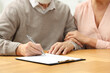 © New Africa - Senior couple signing Last Will and Testament at wooden table, closeup