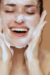© Alliance - smiling young female with foaming face wash washing face