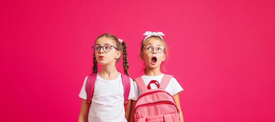 Schoolgirl girls in glasses on a pink background look at the camera. Banner with place for test. End of school, start of vacation. Start of school. Back to school. Bright clothes on girls