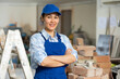 Portrait of positive builder woman in blue overalls next to a stepladder