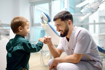 Friendly dentist greets cute toddler boy in office. Doctor encouraging with small child patient and giving him 