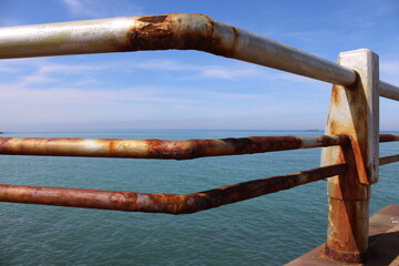 A rusty fence with a blue sea in the background.Rusty iron railing, beautiful sea and sky landscape view between rusty railing gap.