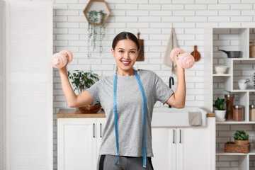 Poster - Young woman with dumbbells and measuring tape in kitchen. Weight loss concept