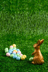 Wall Mural - Happy Easter, gold easter bunny and pastel colored candy coated Easter eggs on artificial green grass
