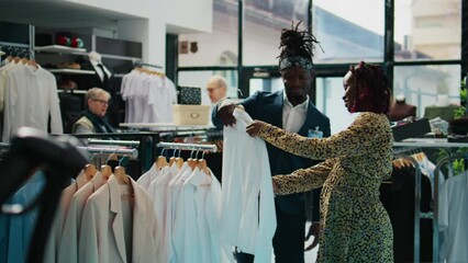 Wall Mural - African american worker showing white shirts to pregnant woman, helping her to choose the right size to buy on discount. Store assistant recommending clothes from designer brands. Camera B.