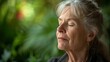 A closeup of a senior womans face as she participates in a guided breathing exercise her expression serene and her mind centered with a backdrop of calming greenery.