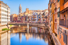 Girona, Spain - Medieval Houses On The Banks Of The River Onyar, And The Pont De Sant Agusti, And The Bell Tower Of Sant Feliu Collegiate Church, Girona, Catalonia, Spain.