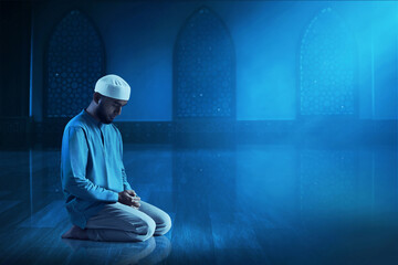 Wall Mural - Young asian muslim man with beard praying in the mosque window arch at dark night