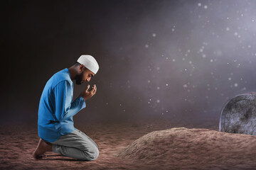 Wall Mural - Portrait of sad crying young asian muslim man with beard praying on graveyard cemetery