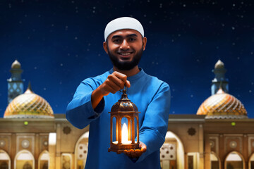 Poster - Portrait of handsome young asian muslim man with beard holding arabic lantern and smiling at beautiful blue night sky with star