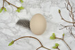 Minimalist easter decoration: egg, feather, brunches and leaves on a marble table. Top view. Scandinavian style.