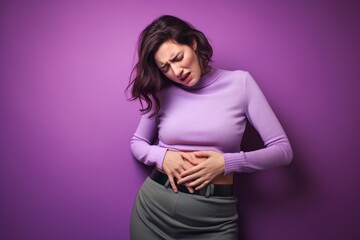 A woman in her 30s holding her abdomen with discomfort written on her face, against a solid pale purple background, conveying the agony of her stomach cramps