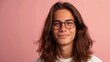 © Z A C - Young person with long brown hair wearing glasses smiling against a pink background.