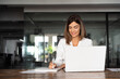 © Stock 4 You - 40s mid age European business woman CEO working on laptop sitting at table workspace, making notes in office. Smiling Latin Hispanic mature adult professional businesswoman using pc digital computer