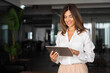 © Stock 4 You - Latin Hispanic mature adult professional business woman looking at online trade app. European businesswoman CEO holding digital tablet using fintech tab application standing at workplace in office.