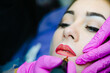 Tattoo lips making. Professional cosmetician applying permanent makeup.
