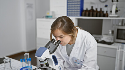 Canvas Print - In the heart of science, young attractive blonde woman scientist intently working with microscope at laboratory, brewing discoveries through analysis