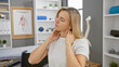 © Krakenimages.com - A young blonde woman examines her neck in a medical clinic filled with shelves and anatomical posters