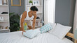 A young hispanic man arranges pillows in a modern bedroom at home, showcasing a tidy and stylish interior.