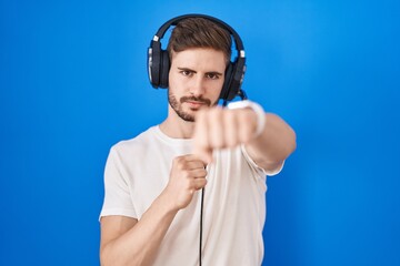 Poster - Hispanic man with beard listening to music wearing headphones punching fist to fight, aggressive and angry attack, threat and violence