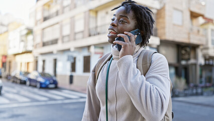 A joyful young black woman with dreadlocks talking on a phone, strolling on a sunny urban city street.