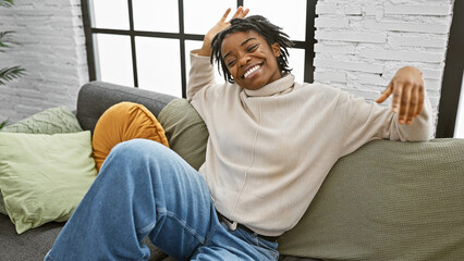 Poster - African american woman with dreadlocks smiling on a sofa in a cozy living room interior.