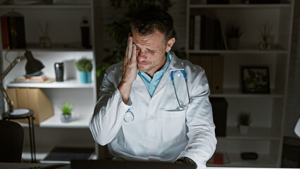 Sticker - A stressed doctor in a clinic holding his head in frustration at his workplace.