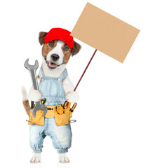 Poster - Funny Jack russell terrier puppy wearing red cap and denim overalls with tool belt holds wrench and shows empty placard. isolated on white background