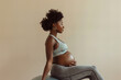 © Denis - Beautiful pregnant black woman in a sports bra and leggings sitting on a stability ball on a light beige background. Pregnancy exercise and healthy lifestyle.