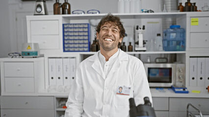 Wall Mural - Smiling man in lab coat standing inside a laboratory with equipment and shelves