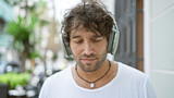 Fototapeta Panele - A handsome young man listening to music with headphones on an urban city street, exuding a relaxed vibe.