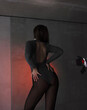 © NASTYA PALEHINA - young teen girl in shiny silver bodysuit is standing fashion from the back with hands near waist and looking apart on gray wall background in loft interior with red light. fashion concept, free space