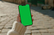 Mockup of an iPhone with a green screen, hand horizontally holding the iPhone, on a city street