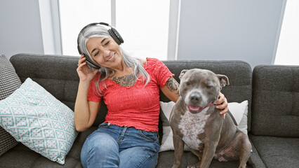 Poster - Confident grey-haired middle age woman joyfully dancing to music while sitting with her pet dog on the sofa at home