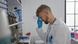 © Krakenimages.com - A stressed young man in a lab coat exhibiting a headache against a clinical laboratory backdrop