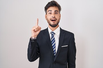 Sticker - Young hispanic man with tattoos wearing business suit and tie pointing finger up with successful idea. exited and happy. number one.