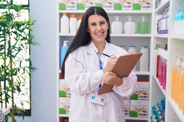 Sticker - Young beautiful hispanic woman pharmacist writing on document at pharmacy