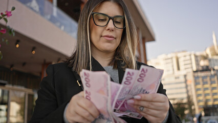 An adult hispanic woman in glasses counts turkish lira banknotes on a sunny istanbul street