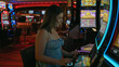 © Krakenimages.com - Smiling woman playing a slot machine at a casino, gambling environment illuminated by colorful neon lights.