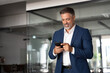 © Stock 4 You - Smiling mature Latin or Indian businessman holding smartphone in office. Middle aged manager using cell phone mobile app. Digital technology application and solutions for business success development.