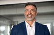 © Stock 4 You - Headshot close up portrait of indian or latin confident mature good looking middle age leader, ceo male businessman in suit on office background. Handsome hispanic senior business man smiling dreaming