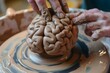 hands sculpting a clay brain on a pottery wheel